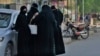 Women wearing hijabs stand along a street in Kabul on May 7, 2022.