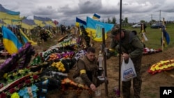 Two national guard visit the grave of a late soldier in Kharkiv cemetery, eastern Ukraine, May 22, 2022.