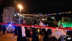 Sejumlah warga ultra ortodoks Yahudi tampak berdiri di belakang garis polisi di lokasi penikaman di Kota Elad, Israel, pada 5 Mei 2022. (Foto: AP/Maya Alleruzzo)