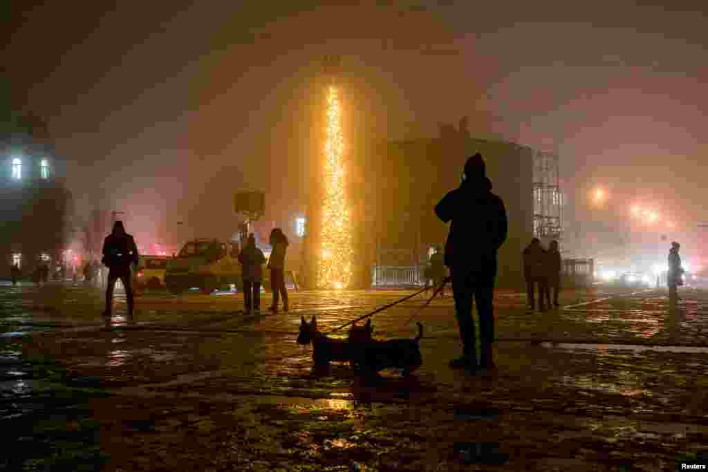 People walk past a Christmas tree during heavy fog at the Sofiyska Square in Kyiv amid Russia's invasion of Ukraine, Dec. 17, 2022.