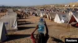 Seorang anak perempuan membawa galon berisi air minum ke area kamp pengungsi yang terdampak oleh banjir di Sehwan, Pakistan, pada 30 September 2022. (Foto: Reuters/Akhtar Soomro)