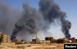 FILE - A man walks while smoke rises above buildings after aerial bombardment in Khartoum, Sudan, on May 1, 2023, two weeks after Sudan’s national army began fighting the rival Rapid Support Forces militia.