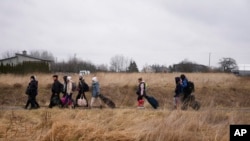 FILE - Orang-orang berjalan dengan barang-barang mereka di perbatasan Medyka, Polandia, saat melarikan diri dari Ukraina, 5 Maret 2022.