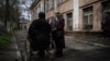 An elderly woman stands beside a man in a wheelchair outside a shelter for internally displaced people, in Dnipro, Ukraine, April 16, 2022.