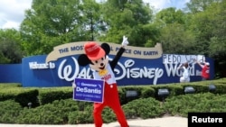 Seseorang yang mengenakan kostum tikus menari sambil memegang poster Gubernur Ron DeSantis dalam aksi protes para pendukung RUU "Don't Say Gay" yang didukung Partai Republik Florida di luar Walt Disney World, Orlando, Florida, 16 April 2022. (REUTERS/Octavio Jones)