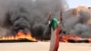 A protester wearing a Sudanese flag flashes the victory sign in front of burning tires and debris on Road 60, near Khartoum's army headquarters, in Khartoum, Sudan, June 3, 2019.