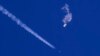 FILE - In this photo provided by Chad Fish, the remnants of a large balloon drift above the Atlantic Ocean, just off the coast of South Carolina, with a fighter jet and its contrail seen below it, Feb. 4, 2023.