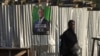 A woman walks past a campaign poster of a presidential candidate Alassane Ouattara of the ruling RHDP coalition, in Attecoube district, Abidjan, Ivory Coast, Oct. 23, 2020. 