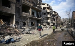 People walk through the damage, after an air raid in the besieged town of Douma, Eastern Ghouta, Damascus, Syria, Feb. 23, 2018.