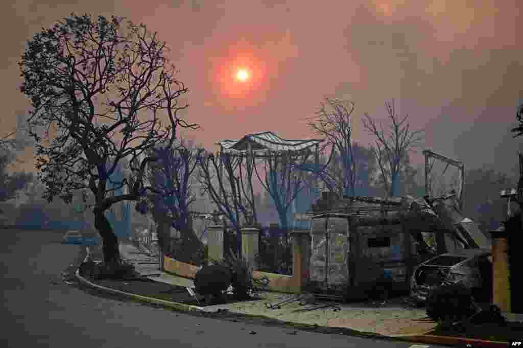 The sun is seen behind smoke above charred structures and vehicles after the Palisades Fire raged in Pacific Palisades, California, Jan. 8, 2025. At least five people have been killed in wildfires rampaging around Los Angeles, officials said, with firefighters overwhelmed by the speed and ferocity of multiple blazes.