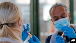 Doctor Anil Mehta and Apprentice Nursing Associate Ellie Bull prepare syringes with doses of the AstraZeneca vaccine at the Welcome Centre in Ilford, east London, Friday, Feb. 5, 2021. Mehta and his small team of doctors and nurses have been pitching up at homeless centers in his