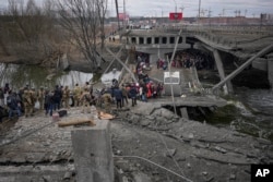 Orang-orang menyeberang di jalur improvisasi di bawah jembatan yang dihancurkan oleh serangan udara Rusia, saat melarikan diri dari kota Irpin, Ukraina, 5 Maret 2022. (Foto: AP)