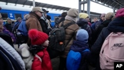FILE - Parents accompany children and teenagers as they board a train after leaving Kyiv's Central Children's Hospital, following its evacuation, in Kyiv, Ukraine, Monday, March 7, 2022.