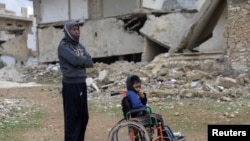 FILE - Mahmoud Madarati, 55, poses as he stands near his son whose leg and hand were amputated after sustaining injuries by what Mahmoud says was shelling from government-held areas, northern Syria, March 3, 2022. 