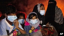 FILE - Ethnic Rohingya women and children sit by a fire on a beach after their boat was stranded on Idaman Island in East Aceh, Indonesia, June 4, 2021, after leaving a refugee camp in Bangladesh.