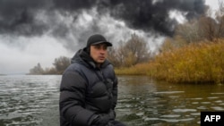 A fisherman sails his boat on the Dnipro River as black smoke rises after an attack on an oil reserve in Kherson, on Nov. 20, 2022, amid the Russian invasion of Ukraine.