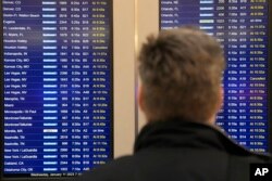 Steve Gasser dari Chicago melihat layar informasi penerbangan di Bandara Midway Chicago yang melaporkan penundaan penerbangan akibat gangguan pada komputer FAA di Administrasi Penerbangan Federal, yang menyebankan terdundanya penerbangan di seluruh AS Rabu, 11 Januari 2023. (AP/Charles Rex Arbogast)