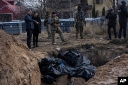 Orang-orang berdiri di samping kuburan massal di Bucha, di pinggiran Kyiv, Ukraina, Senin, 4 April 2022. (Foto: AP/Rodrigo Abd)