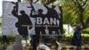 Personel Pasukan Aksi Cepat (RAF) berjaga di samping spanduk yang dipasang oleh para pendukung dan aktivis Partai Bharatiya Janata (BJP) yang berkuasa di India selama protes menuntut larangan organisasi Front Populer India (PFI) di New Delhi pada 28 Februari 2021 (Foto: AFP)