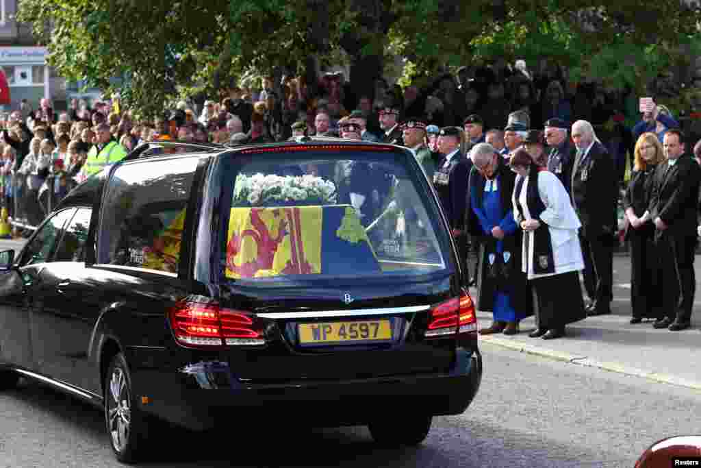 People pay respects to Queen Elizabeth as the hearse carrying her coffin passes through the village of Ballater, near Balmoral, Scotland, Sept. 11, 2022.
