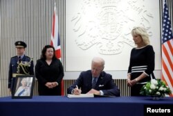 Presiden AS Joe Biden menandatangani buku belasungkawa saat ibu negara AS Jill Biden memandang foto Ratu Elizabeth, raja terlama yang memerintah Inggris dan tokoh negara selama tujuh dekade, meninggal pada usia 96, di Kedutaan Besar Inggris, di Washington, AS, 8 September, 2022. (REUTERS/Evelyn Hockstein)