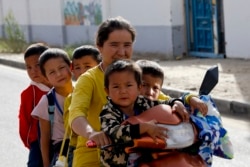 Seorang wanita dan anak-anak Uighur duduk di atas sepeda roda tiga sepulang sekolah di Unity New Village di Hotan, di wilayah Xinjiang, China barat, 20 September 2018. (Foto: AP)