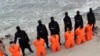 FILE - Captives in orange jumpsuits — purported to be Egyptian Christians —kneel in front of armed Islamic State militants along a beach said to be near Tripoli, in this still image from an undated video made available on social media, Feb. 15, 2015.