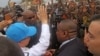 U.N. Secretary-General Ban Ki-moon, in a cap, waving at people kept back by a wire fence, as he walks surrounded by U.N. security personnel in a secured location in Bangui, Central African Republic, April 5, 2014.