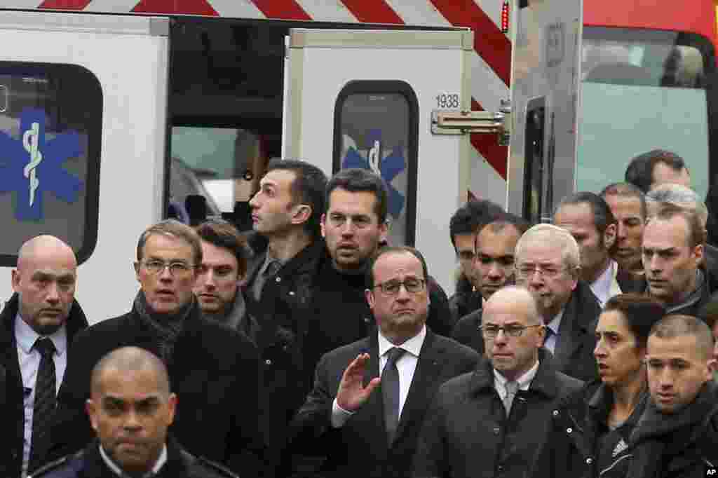 French President Francois Hollande, center, flanked with security forces gestures, as he arrives outside the French satirical newspaper Charlie Hebdo's office, in Paris, Jan. 7, 2015.