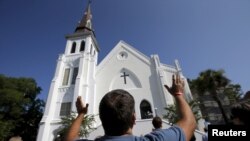 Robin Goolfby, salah seorang jemaat yang tidak bisa masuk akibat penuhnya gereja, mengangkat tangannya di depan gereja Emanuel AME mengikuti kebaktian di Charleston, South Carolina, 21 Juni 2015. 