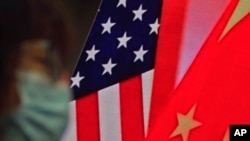 In this Feb. 22, 2021, file photo, a woman wearing a face mask sits near a screen showing China and U.S. flags as she listens to a speech on China-U.S. relations.