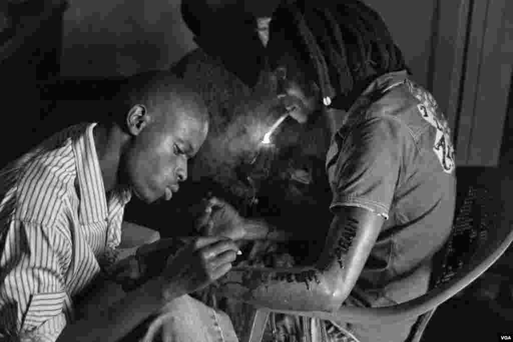Negenzi Ali (left), age 23, makes a tattoo of a Rwandan genocide slogan "never again" on Tomy's arm. Negenzi Ali says "I don't care about HIV transmission through my needles. Giporoso is killing our generation softly." Giporoso, Kigali, Rwanda, Nov. 5, 2013.