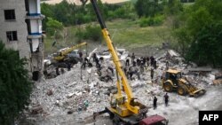 Firefighters and members of a rescue team search the debris after a building was partially destroyed following shelling, in Chasiv Yar, eastern Ukraine, on July 10, 2022. - A Russian missile struck an apartment building in Chasiv Yar, in eastern Ukraine o