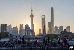 Pengendara sepeda, ada pula yang berfoto selfie sambil beristirahat menghadap cakrawala matahari terbit di Pudong, pusat keuangan dan komersial China, di Shanghai, China pada Jumat, 3 November 2023. (Foto: via AP)