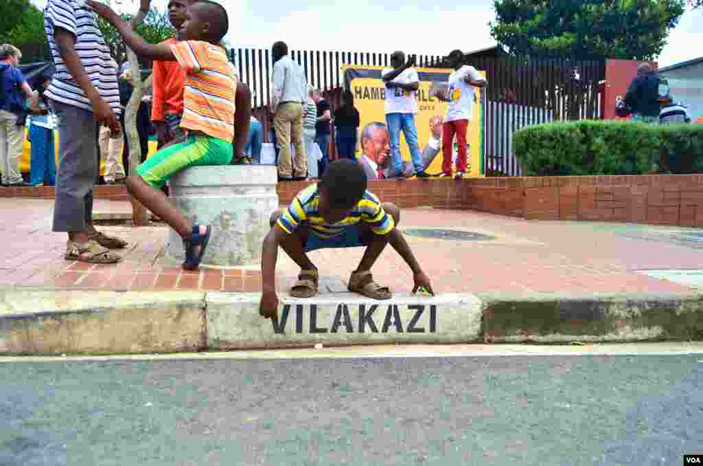 A young boy traces the letters on the Vilakasi Street sign outside of Nelson Mandela's home in Soweto, now the Nelson Mandela National Museum, Dec. 12, 2013. (Peter Cox for VOA)