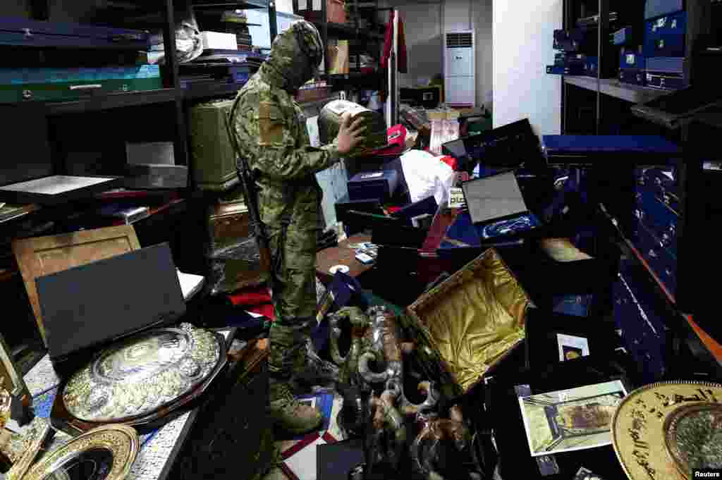 A rebel fighter holds and looks at personal souvenirs of Syrian President Bashar al-Assad at one of the rooms at Presidential Palace known as Qasr al-Shaab "People's Palace," in Damascus.