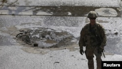 A NATO soldier stands at the site of a suicide car bomb blast in Kabul, Afghanistan, Oct. 11, 2015.