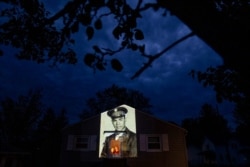 An image of veteran Samuel Melendez is projected onto the home of his nieces, Janet Ramirez, right, and Mary Perez, as they look out a doorway in Chicopee, Mass., May 17, 2020.