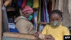 FILE - A woman who trades in fabrics, and her child, wear face masks to rotect against the coronavirus, in her shop inside Lilongwe City market, in Lilongwe, Malawi, May 18, 2020.