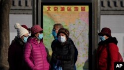 Commuters wearing face masks to protect against the coronavirus wait for their buses at a bus stand in Beijing, China, Dec. 19, 2021. 