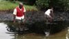 FILE - Men walk in an oil slick covering a creek near Bodo City in the oil-rich Niger Delta region of Nigeria, June 10, 2010.