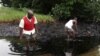 FILE - Men walk in an oil slick covering a creek near Bodo City in the oil-rich Niger Delta region of Nigeria, June 10, 2010.
