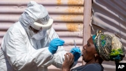 FILE - A woman opens her mouth for the heath worker to collect a sample for coronavirus testing during the screening and testing campaign aimed to combat the spread of COVID-19 at Lenasia South, south Johannesburg, South Africa, April 21, 2020.