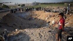 FILE - A barefoot Palestinian boy looks into a crater made in an overnight Israeli missile strike, that destroyed a house and killed nine members of the Abu Malhous family, in Deir al-Balah, central Gaza, Nov. 14, 2019.