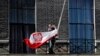 FILE - A man lowers the Polish national flag outside the Polish Embassy, in London, April 10, 2010. Economists warn that any new restrictions on workers from mainland EU countries may cause labor shortages, hurt Britain’s economy.