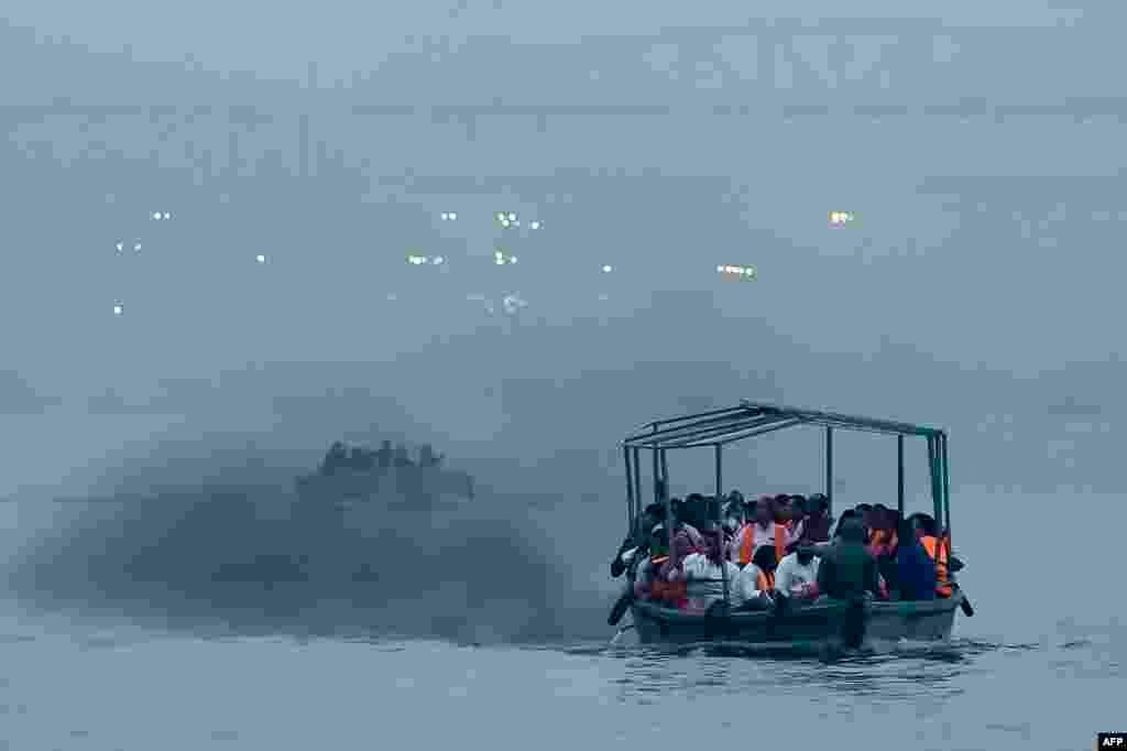 People ride a motor boat emitting smoke, across river Ganges in Varanasi, India.