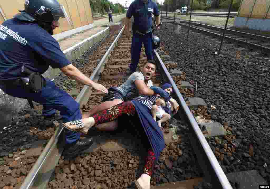 Polisi Hungaria berdiri dekat keluarga migran yang hendak melarikan diri di stasiun kereta api di kota Bicske (3/9). Ada kamp pengungsi dan pencari suaka di kota itu. (Reuters/Laszlo Balogh)