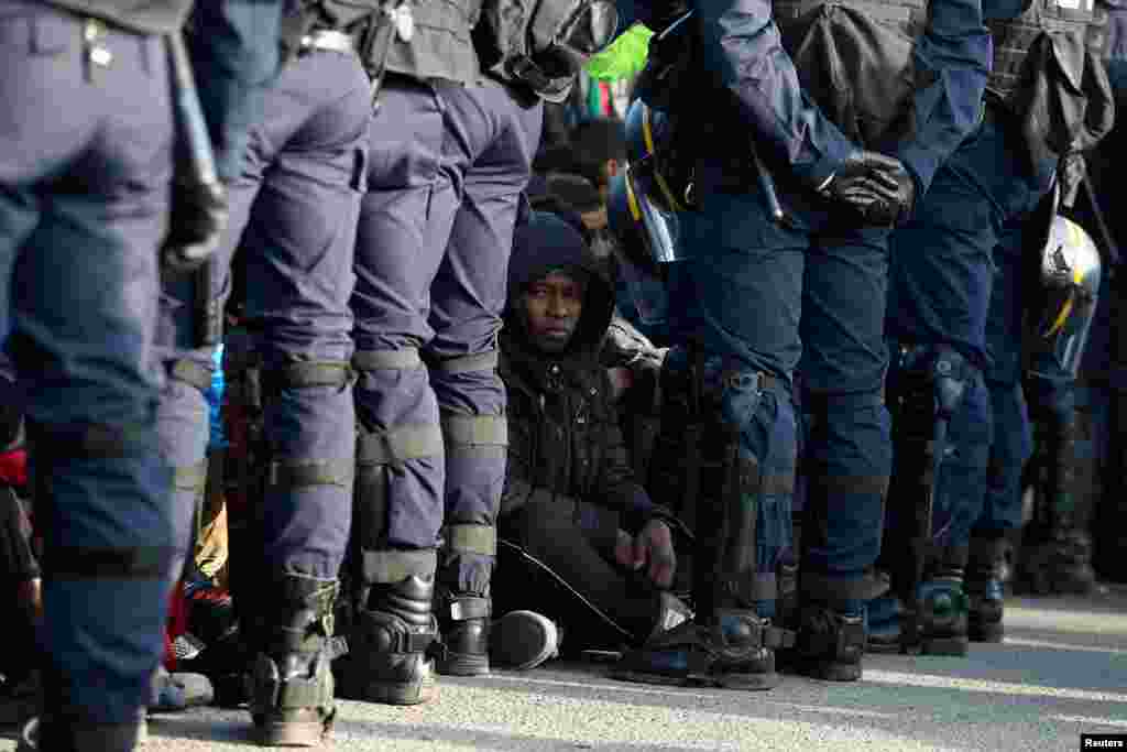 French police stand near as migrants wait in front of a processing center to be registered on the second day of their evacuation and transfer to reception centers in France, during the dismantlement of the camp called "the jungle" in Calais, France, Oct.