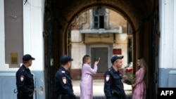 Beberapa polisi yang sedang berpatroli melintas di depan dua perempuan Rusia yang saling berfoto di depan pintu masuk, di Kota Nizhny Novgorod, Rusia yang sedang berlangsung turnamen sepak bola Piala Dunia 2018, 21 Juni 2018.