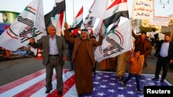 FILE - Iraqi people walk on a U.S. flag in a protest after an airstrike at the headquarters of Kataib Hezbollah militia group in Qaim, in the holy city of Najaf, Iraq, Dec. 30, 2019.